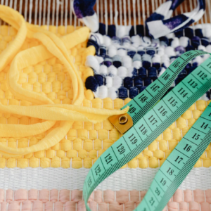 A vibrant weaving project with a measuring tape and threads on a loom.