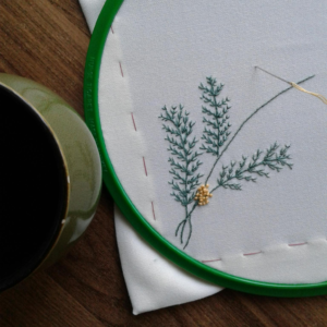 Close-up of a delicate leaf embroidery in progress with threads on fabric, showcasing craftsmanship.